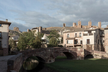 Obraz premium a historic town with stone buildings, an arched bridge, and distant castles under a partly cloudy sky