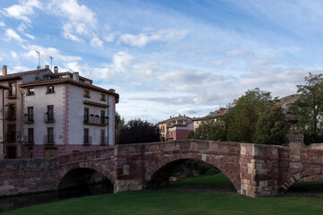Naklejka premium a scenic view of a stone bridge, green grass, and buildings under a partly cloudy sky