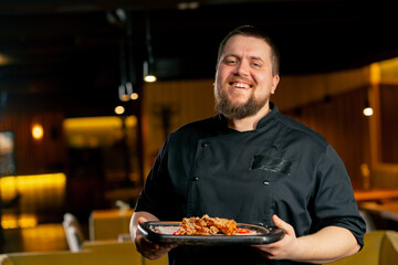 in a restaurant a chef in a black jacket stands smiling with a prepared Chicken wings
