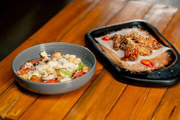 close-up on a wooden table there is a prepared dish of caesar salad in gray plate and chicken wings