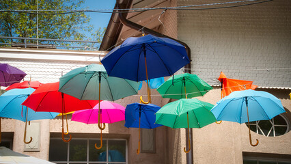 Eine bunte Sammlung von aufgespannten Regenschirmen, die an Leinen gespannt, vor einer Hauswand...