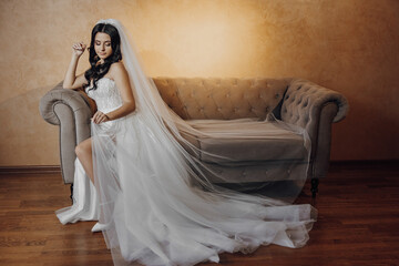 A woman in a wedding dress sits on a couch. She is wearing a veil and a tiara