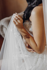A woman is wearing a white wedding dress and holding a veil. She is wearing a ring on her finger
