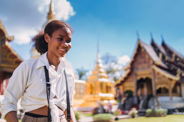 happy black tourist girl taking picture using vintage camera at temple. teenage african american using vintage camera taking temple photo. solo traveler relax doing photo shoot of thailand landmark - Powered by Adobe