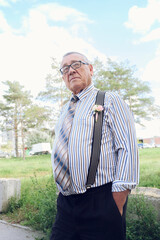 elderly man dressed in a shirt and suspenders on a walk in a city park on a summer day