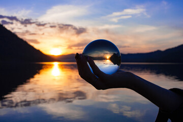 Beautiful scenic view through lens of crystal ball on water horizon at summer sunset. Clouds...