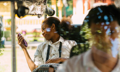 happy traveler black girl using phone on tuk tuk ride. cheerful solo teenage tourist using phone...