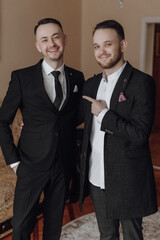 Two men in suits are posing for a picture, one of them pointing to the camera. Scene is lighthearted and fun, as the two men are smiling and enjoying themselves