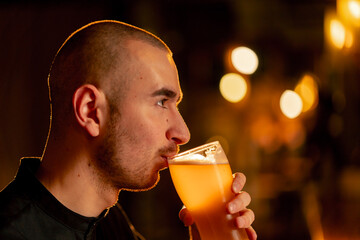 close-up on a wooden bar table guy drinks from a glass of light beer warm lighting light