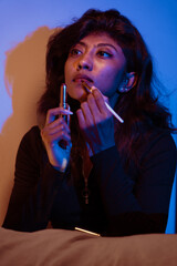 Fototapeta premium A woman is applying lipstick while holding a cigarette