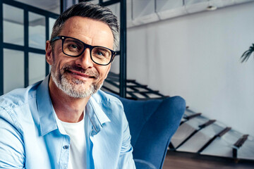 Middle aged bearded glasses man handsome with eyeglasses and blue shirt at home