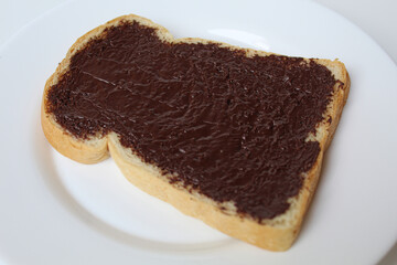 One slice of white bread, covered by chocolate spread, on white plate, isolated on white background. Prepare chocolate sandwich