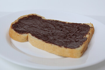 One slice of white bread, covered by chocolate spread, on white plate, isolated on white background. Prepare chocolate sandwich