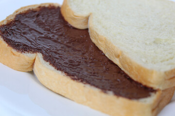 Two slices of white bread with chocolate spread or chocolate jam. Chocolate sandwich. On white plate, isolated on white background
