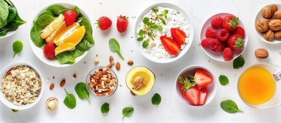 Healthy food concept with breakfast items including muesli, strawberry salad, fresh fruit, orange juice, and nuts laid out on a white background in a flat lay, top view style.