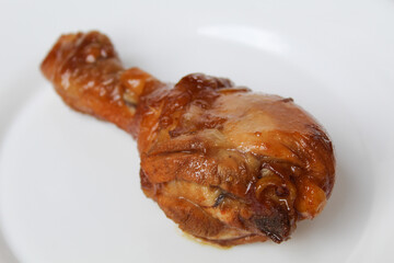 Ayam Kecap, or chicken cooked with sweet soy sauce. One chicken drumstick on white plate, isolated on white background