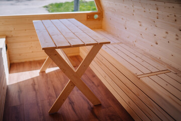 Interior shot showing a simple, natural wood table with X-shaped legs in a wooden cabin.