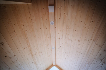 Interior view of a wooden cabin's ceiling featuring a sloped design with two embedded round lights...
