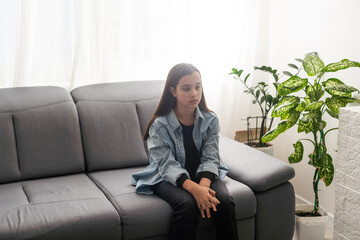 girl wearing blue shirt sitting on couch at home and looking away. Lifestyle child portrait.