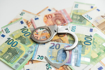 Police handcuffs lies on a set of green monetary denominations of 100 euros. A lot of money forms...