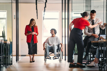Fototapeta premium A business leader with her colleague, an African-American businessman who is a disabled person, pass by their colleagues who work in modern offices