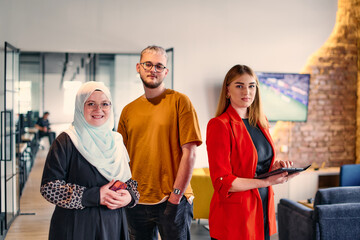 A group of young business colleagues, including a woman in a hijab, stands united in the modern...