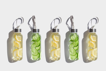 Glass bottles with lemon, cucumber water drink detox at sunlight on white, creative pattern....