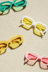 Stylish colored sunglasses on sand background at sunlight, summer fashion collection eyeglasses with colors glass. Summer sale concept in optical store. Top view lifestyle aesthetic photo