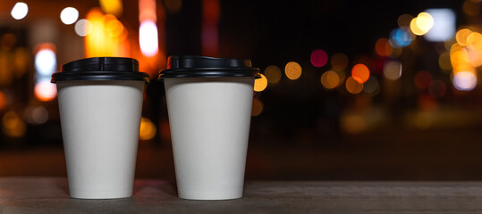 Close-up of two white eco-friendly recycled paper cups with coffee or tea standing on a bench...