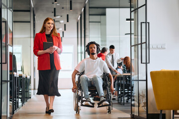 Fototapeta premium A business leader with her colleague, an African-American businessman who is a disabled person, pass by their colleagues who work in modern offices