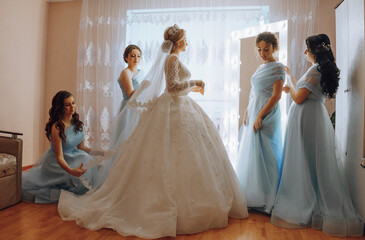 A bride and her bridesmaids are getting ready for the wedding. The bride is wearing a white dress...