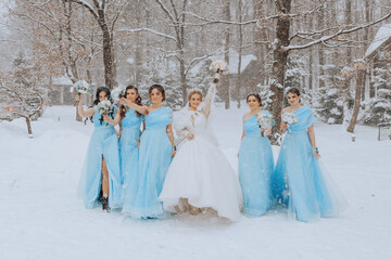 A bride and her bridesmaids are posing for a picture in the snow. The bride is wearing a white...