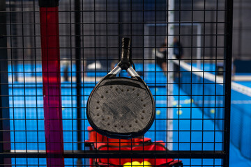 Black professional paddle tennis racket and ball with natural lighting on blue background....