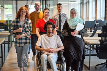A diverse group of young business people congregates within a modern startup's glass-enclosed...