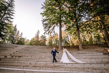 Valmiera, Latvia - August 19, 2023 - Bride and groom holding hands on a wooden amphitheater in a...