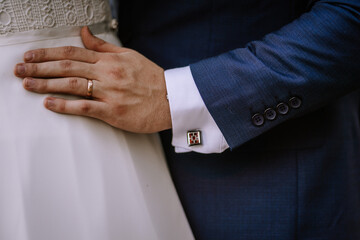 Valmiera, Latvia - August 19, 2023 - Close-up of a groom's hand on a bride's waist, showing his wedding ring, cufflink, and details of their wedding attire.