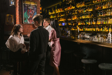 Young guys and ladies speak and drink alcohol in modern pub. Atmospheric pub with variety of...