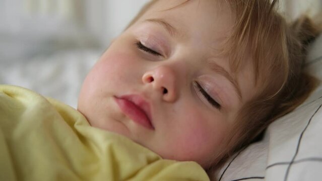 Peaceful adorable baby sleeping on a bed at home. Slumbering little child. Two years old girl sleeps peaceful at domestic room interior background. Serene dream. Cute face close up. Deep kid slumber