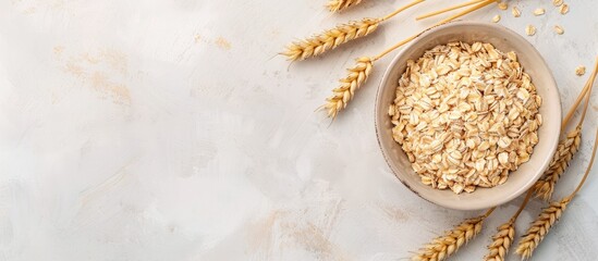 Dry oatmeal in a bowl garnished with wheat ears on a light background, suitable for adding text. Representing the cooking of oats porridge. Viewed from above.