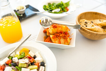 Cabbage rolls in a square plate, Greek salad, juice, bread on a white table. Food tongs