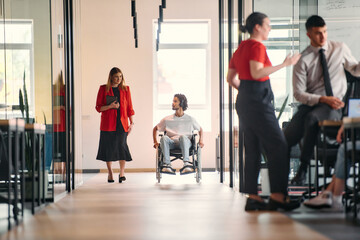 A business leader with her colleague, an African-American businessman who is a disabled person, pass by their colleagues who work in modern offices