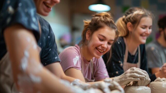Young people enjoying a pottery class, hands covered in clay and smiling brightly.