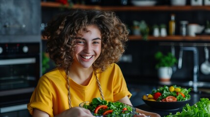 Joyful young woman with curly hair preparing a fresh salad in a modern kitchen.