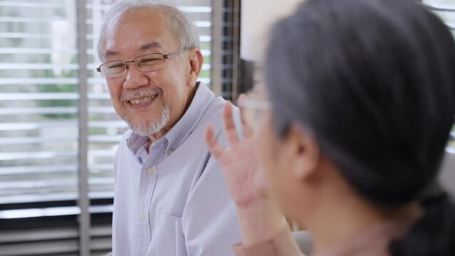 Asian grandfather talking with grandmother sitting on couch in the living room. Senior couple enjoy weekend together at home.
