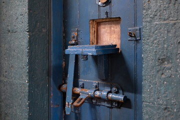 Opened blue painted weathered hatch of an old heavy locked prison door. Selective focus