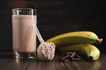 Plastic measuring spoon with whey protein powder, milkshake cocktail in a glass, blended protein...