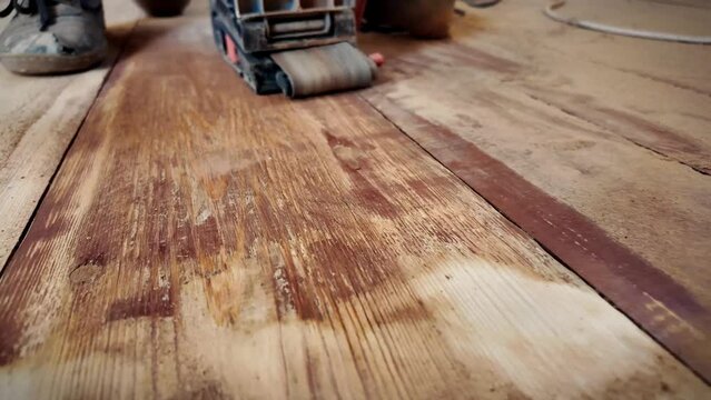 Sanding the floor with a sanding machine close-up video. Dynamic hand movement and dust. Repair work on a wooden floor using power tools. Apartment renovation. Processing old wooden surfaces.