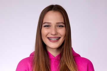 A young woman with braces smiling on a pink background. She exudes confidence and happiness....