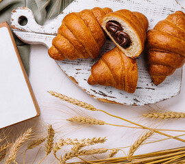 Fresh croissants on rustic wooden board with wheat ears