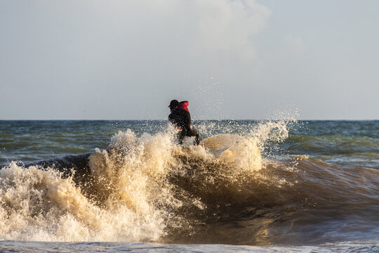 Surfista em cima da onda com espuma à volta numa água acastanhada, céu azul